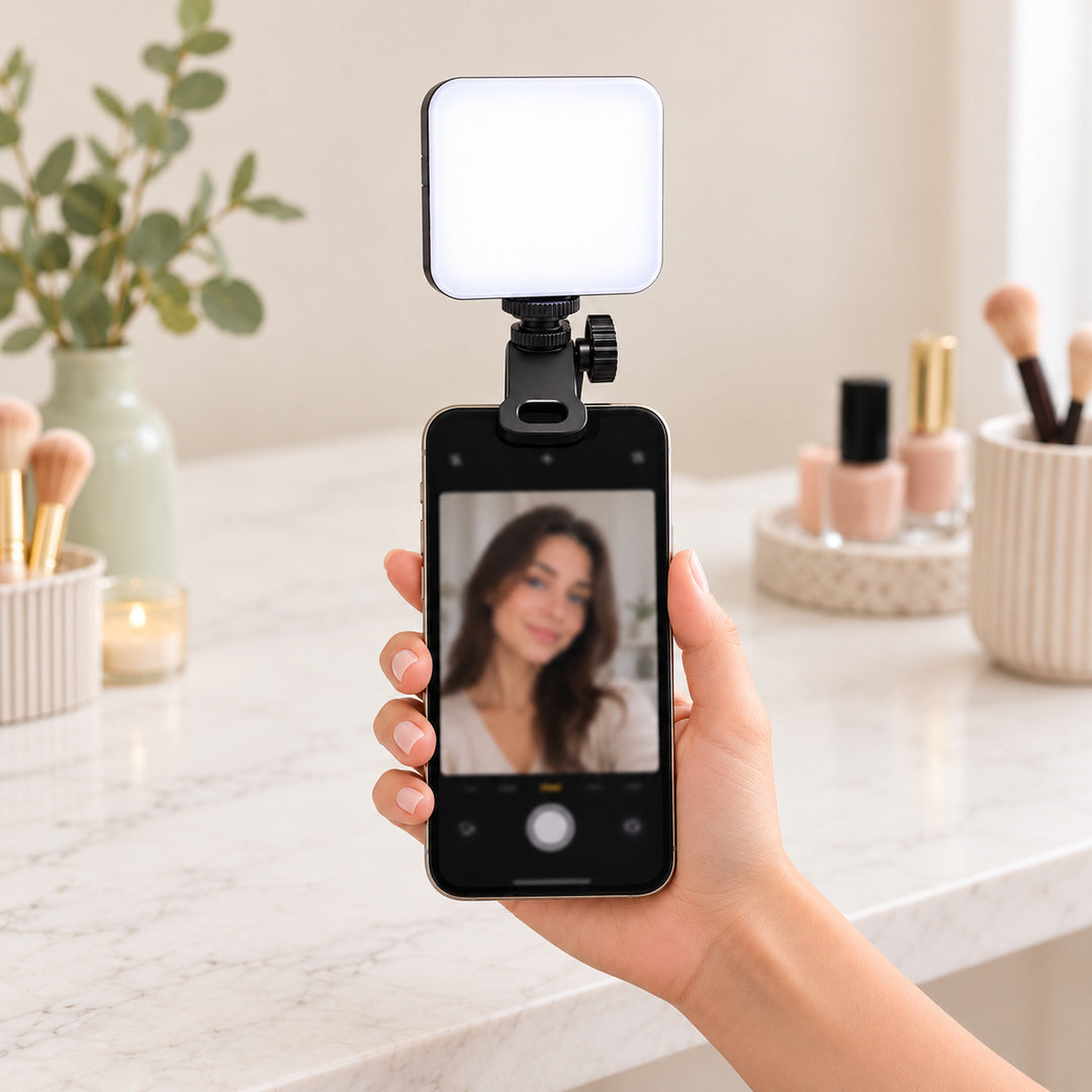 Lampă LED portabilă prinsă cu clema pe marginea superioară a unui laptop, cu panoul luminos orientat spre utilizator, într-un spațiu de lucru cu accesorii beauty.