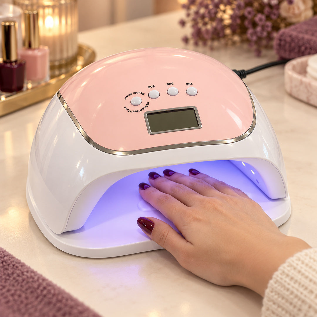 Lampă UV LED BQ V5 roz în funcțiune pe masa de manichiură, cu mâna clientei în interior, unghii burgundy, lumină violetă și cablu de alimentare vizibil, într-un decor de salon.