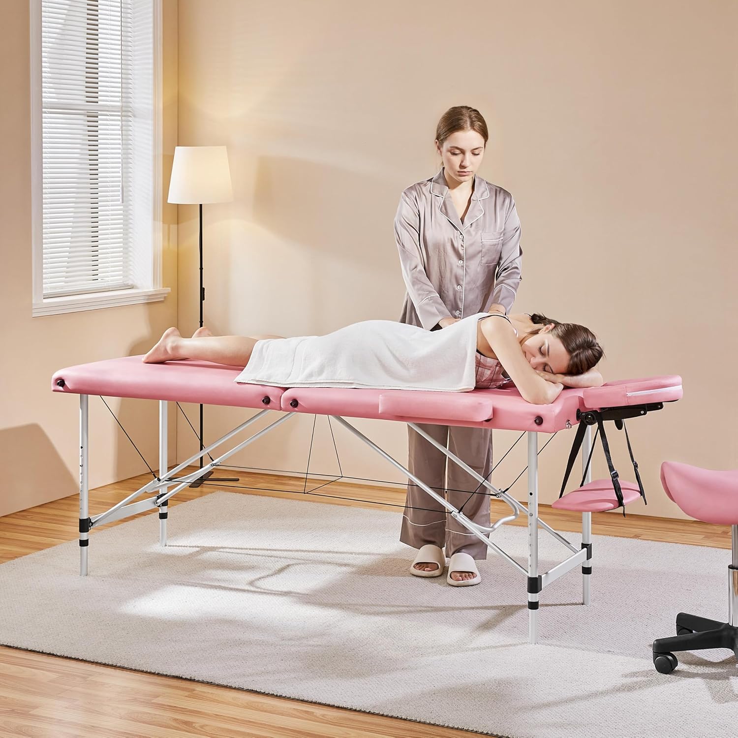 Cadru de prezentare intr-o camera luminoasa unde o terapeuta efectueaza o procedura de relaxare pe o clienta asezata pe patul de masaj profesional roz.